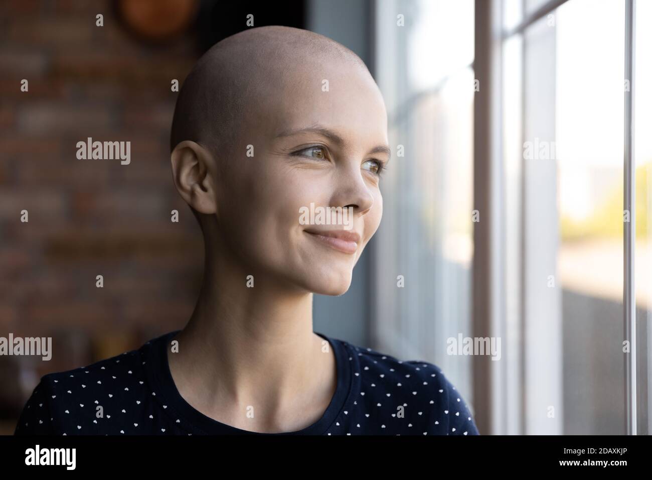 Donna millenaria speranzosa che ha una malattia oncologica sognando vicino a una grande finestra Foto Stock
