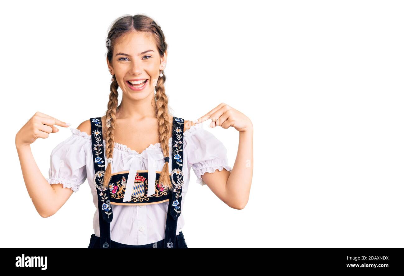 Bella donna caucasica con capelli biondi che indossa abiti tradizionali octoberfest guardando fiducioso con sorriso sul viso, puntandosi con le dita Foto Stock