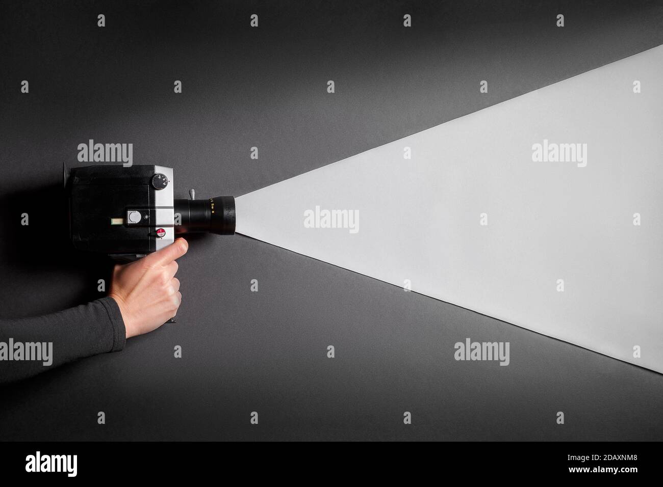 La mano femminile che tiene la vecchia videocamera cinematografica imita il processo di ripresa su uno sfondo nero con una luce grigia che passa attraverso l'obiettivo. Film makein Foto Stock