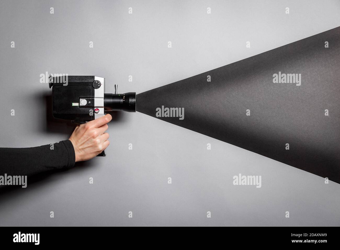 La mano femminile tiene la vecchia macchina fotografica di film di stile imitando il processo di ripresa su uno sfondo nero con una luce nera che arriva attraverso l'obiettivo. Film maki Foto Stock