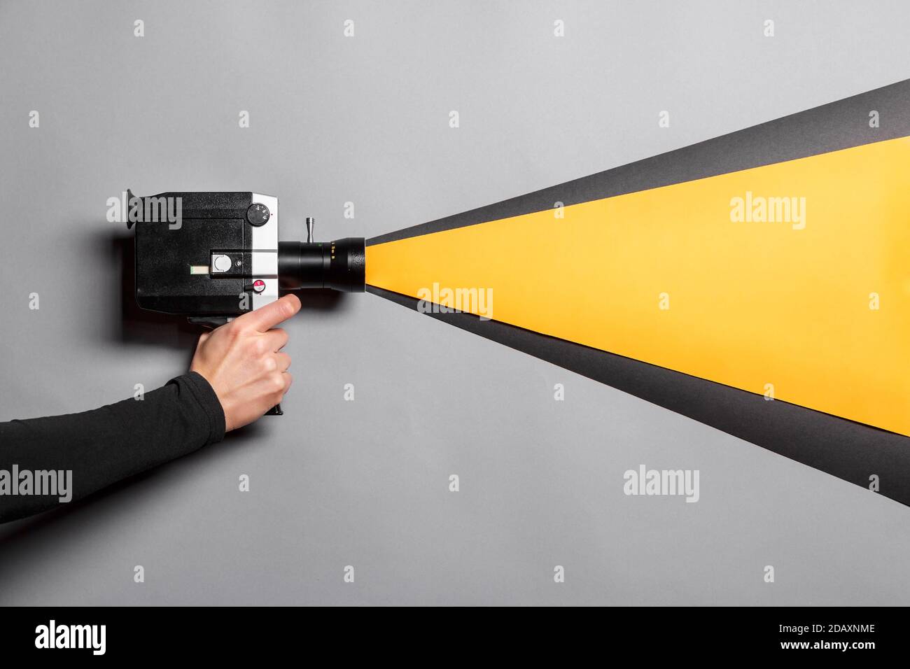La mano femminile tiene la vecchia macchina fotografica di film di stile imitando il processo di ripresa su uno sfondo grigio con una luce nera e gialla che arriva attraverso l'obiettivo. Foto Stock