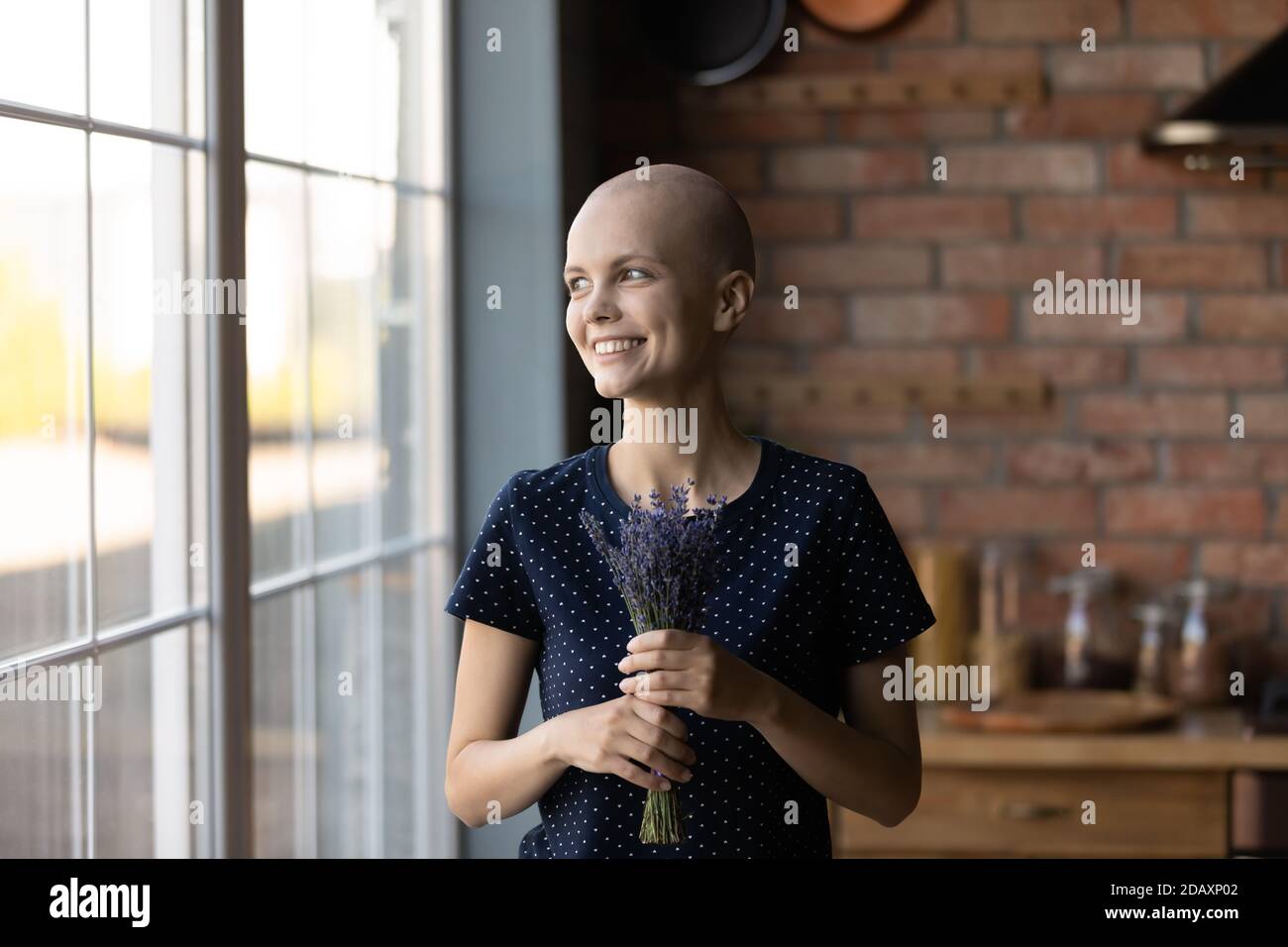 Donna felice che si sta riprendendo dal cancro guardando la finestra che tiene i fiori Foto Stock
