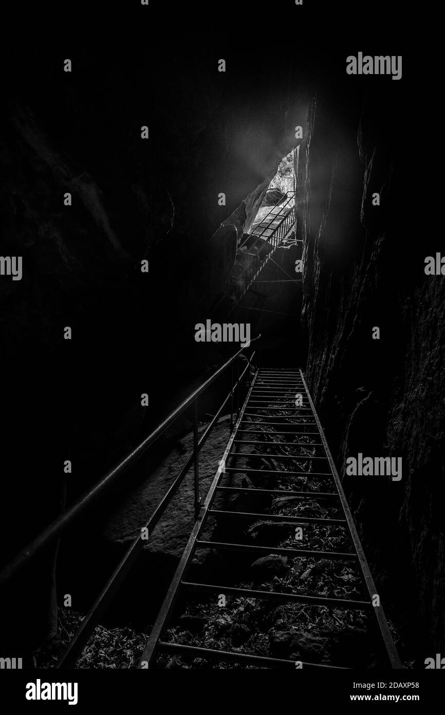 luce alla fine del tunnel di un buio grotta con scaletta Foto Stock