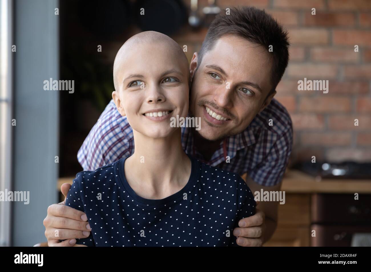Marito affettuoso ottimista che abbuggia le spalle della moglie millenaria paziente di cancro Foto Stock