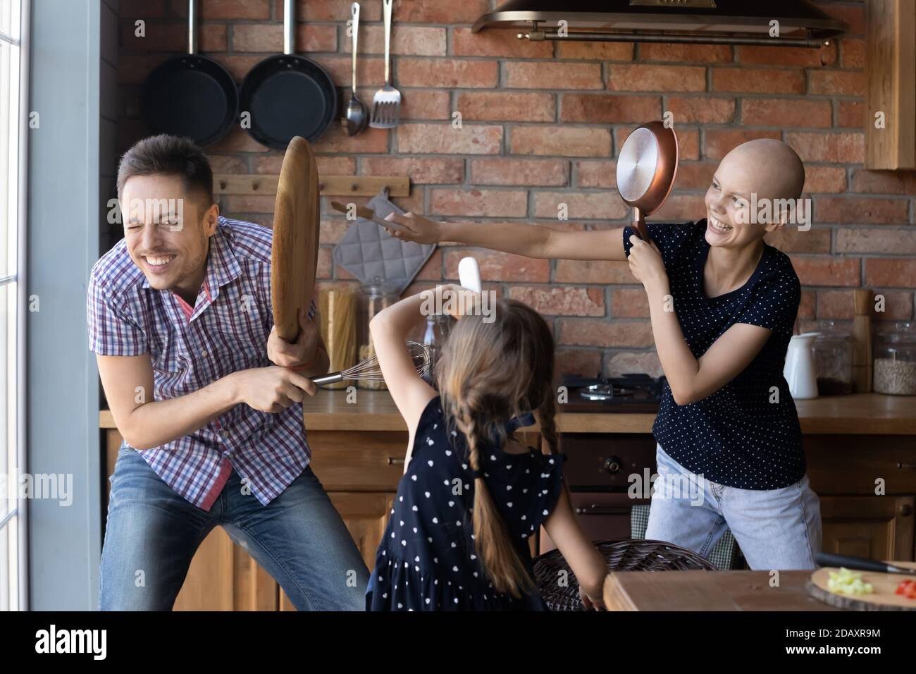 La famiglia di tre membri che si battono sugli utensili da cucina è molto contentata Foto Stock