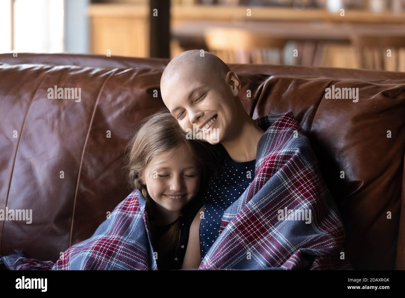 Madre che lotta con oncologia seduta sul divano abbracciando piccola figlia Foto Stock