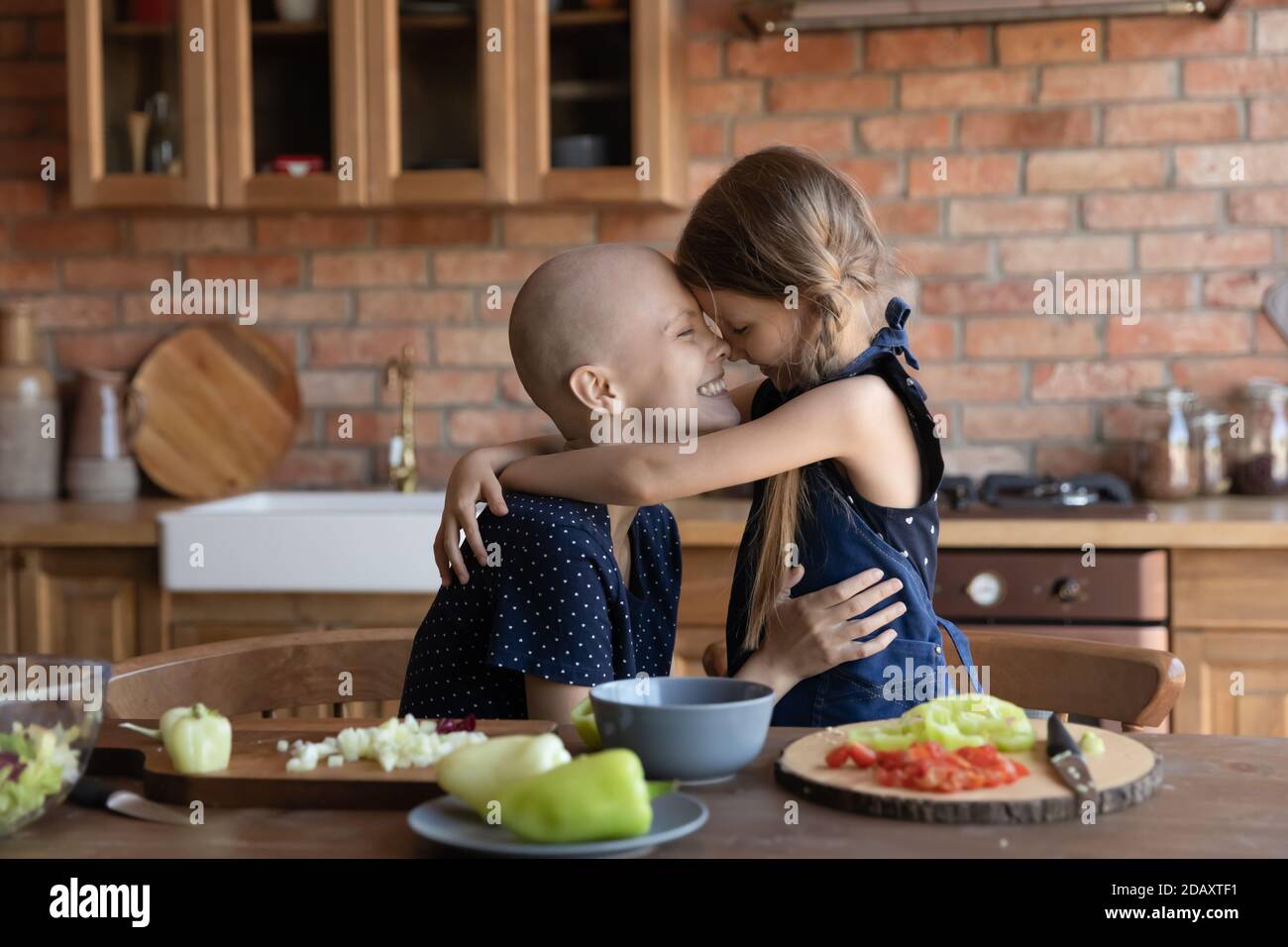 Mamma affettuosa che lotta contro il cancro abbracciando figlia in grembiule cucina Foto Stock