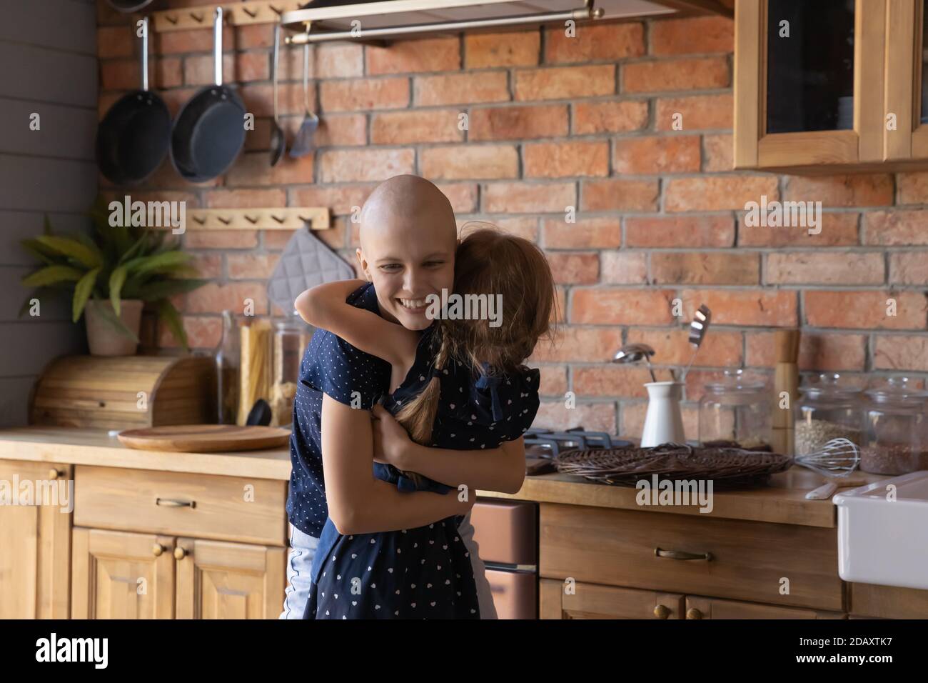 Madre casalinga che ha il cancro abbracciando piccola figlia premurosa in cucina Foto Stock