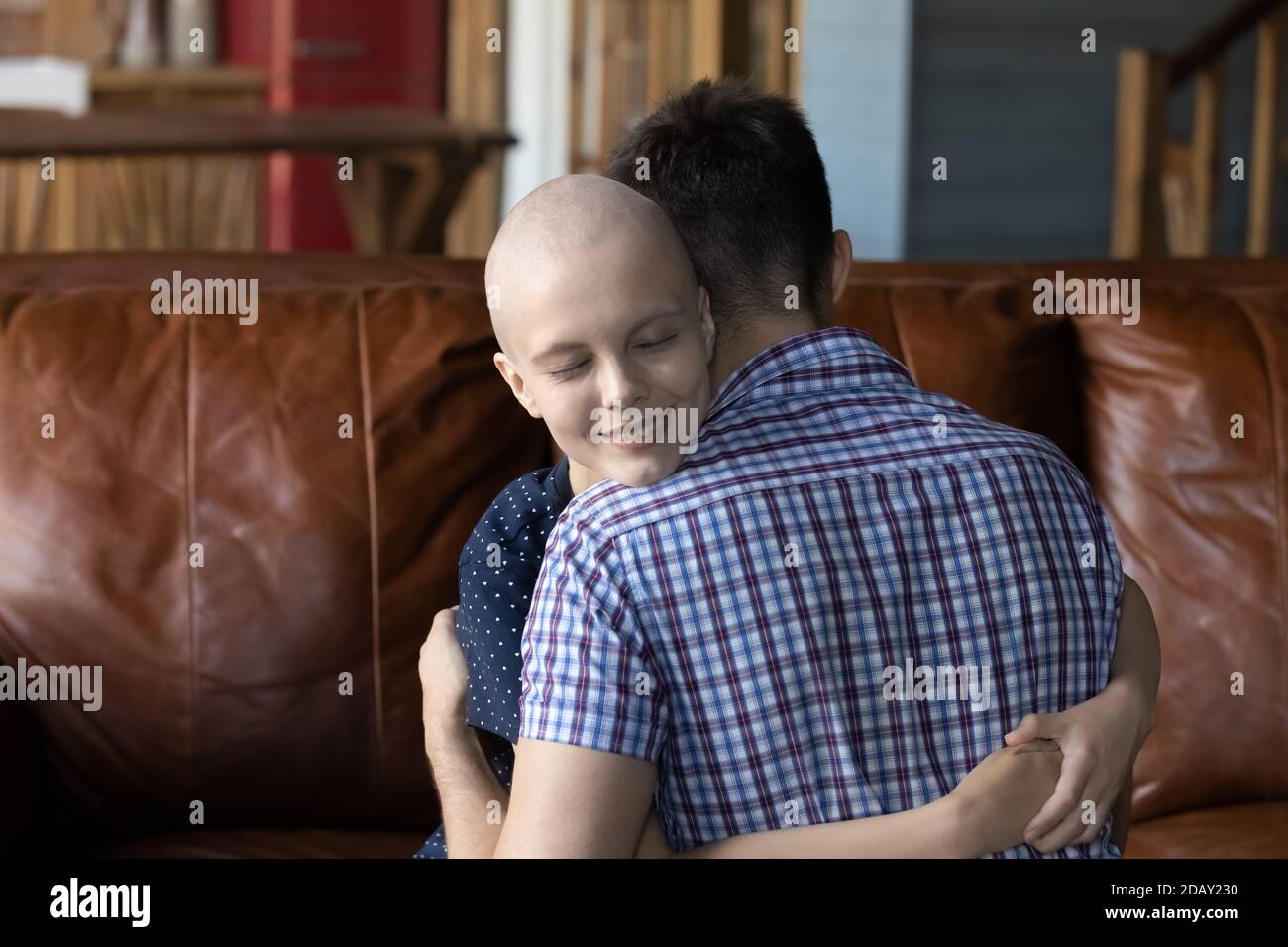 Coppia amorevole dove la donna è paziente di cancro abbracciando sul divano Foto Stock