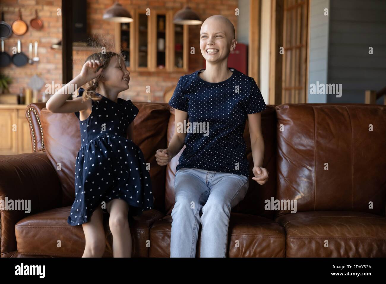 Ridendo madre malata con il cancro che salta sul divano con la figlia Foto Stock