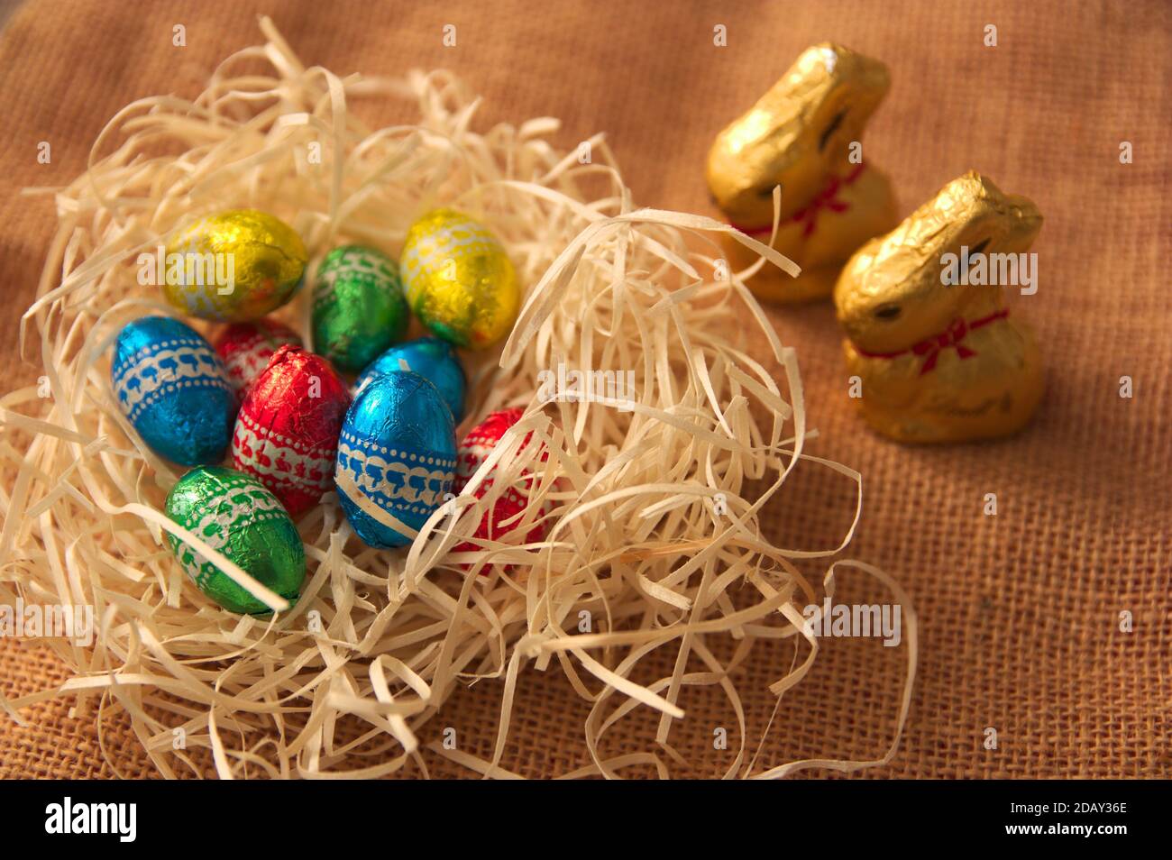 Primo piano di alcune uova di cioccolato che sono in un mucchio di paglia accanto ad alcuni conigli dorati. Sfondo per pasqua Foto Stock