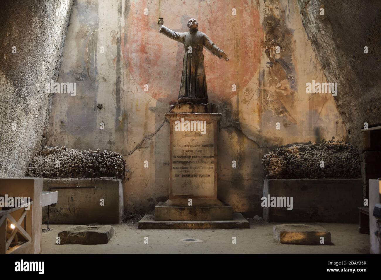 Statua del prete napoletano Gaetano Barbati circondata da ossa umane impilate all'interno del Cimitero delle Fontanelle (Cimitero delle Fontanelle) a Napoli, Campania, Italia. L'ex caserma (ossario) situata in una grotta del distretto di Materdei era il luogo in cui si sviluppò a Napoli il culto spontaneo della devozione ai resti di morti senza nome. I difensori del culto hanno pagato visite ai teschi senza nome nell'ossario per adottarli e persino dare i nomi dei teschi. I teschi adottati furono collocati all'interno della scatola decorata e diventarono oggetto di regolare offerta orante e votiva. Foto Stock