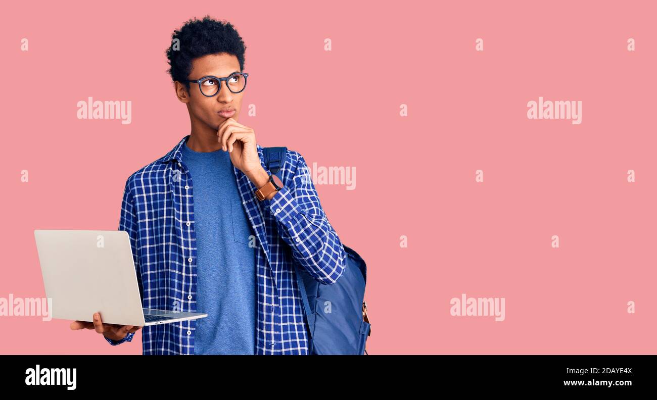 Giovane uomo africano americano che tiene lo zaino dello studente usando il computer portatile faccia seria pensare alla domanda con la mano sul mento, pensieroso circa id confuso Foto Stock
