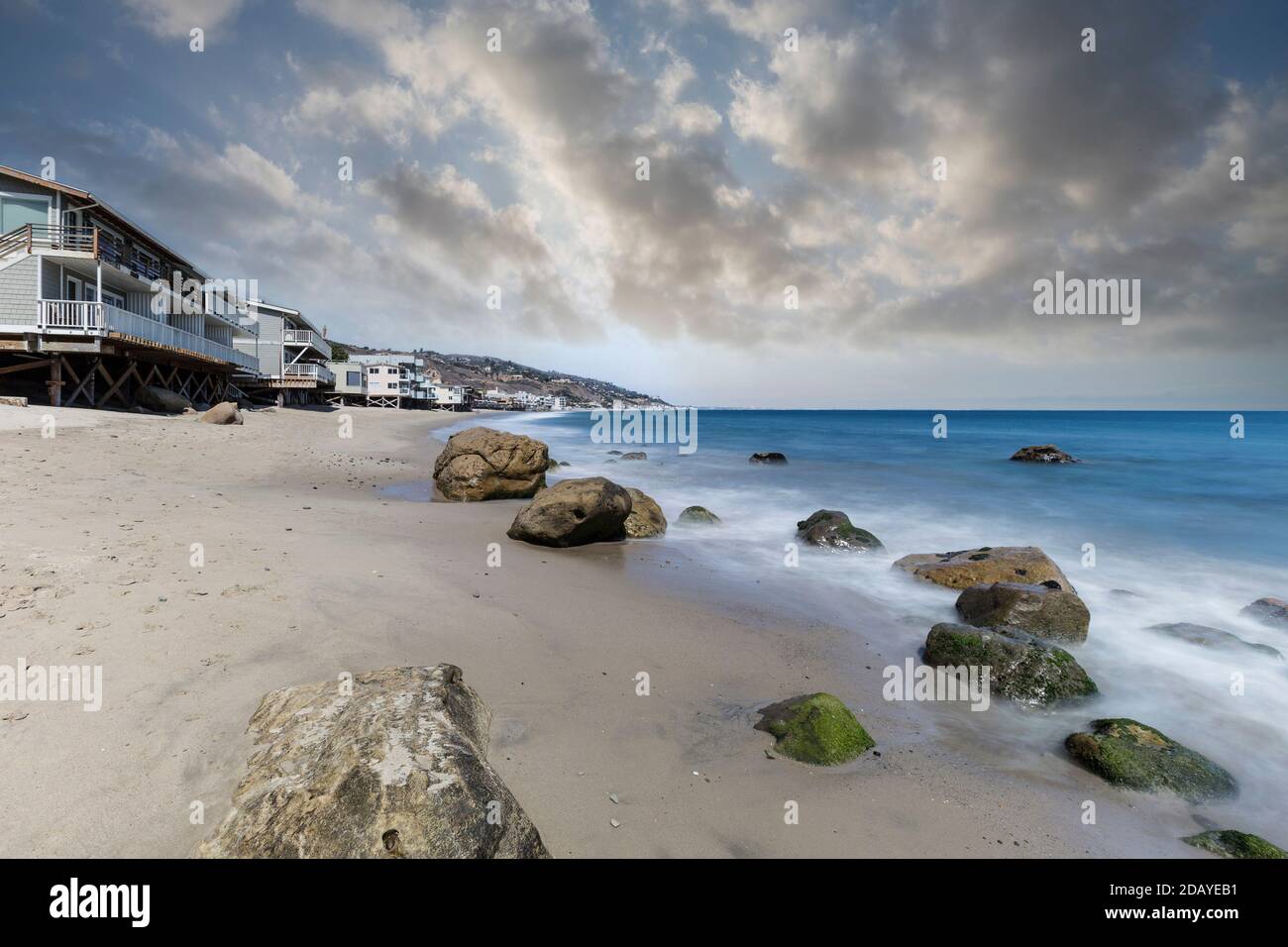 Case fronte oceano con acqua sfocata movimento e cielo nuvoloso a Carbon Beach a Malibu, California. Foto Stock