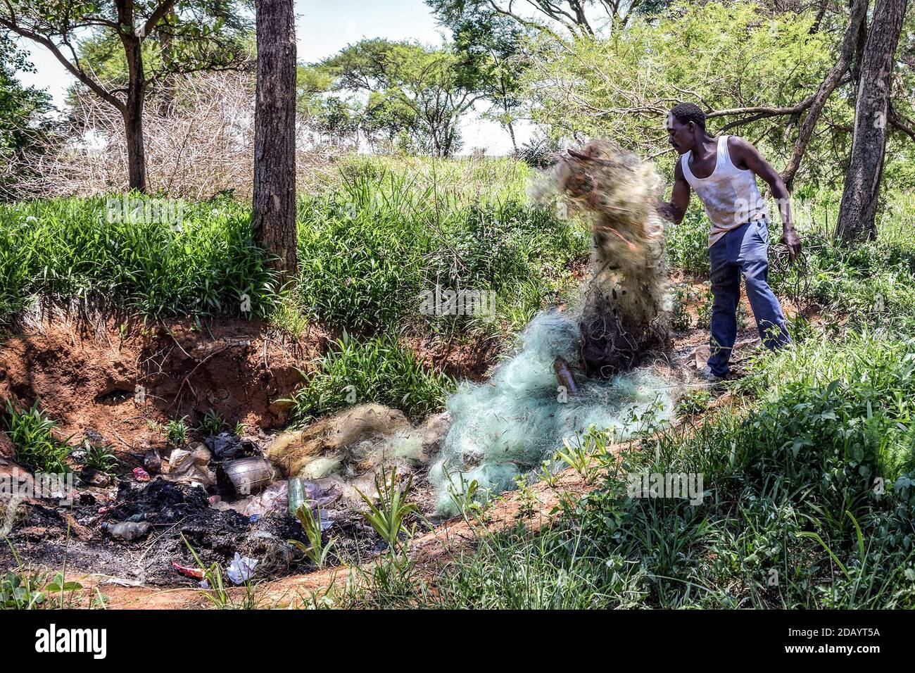 Fungai Kayemba getta una rete di spago usurata in un fossato prima di bruciarla, per evitare di lasciarla nel lago dopo l'uso. Foto Stock