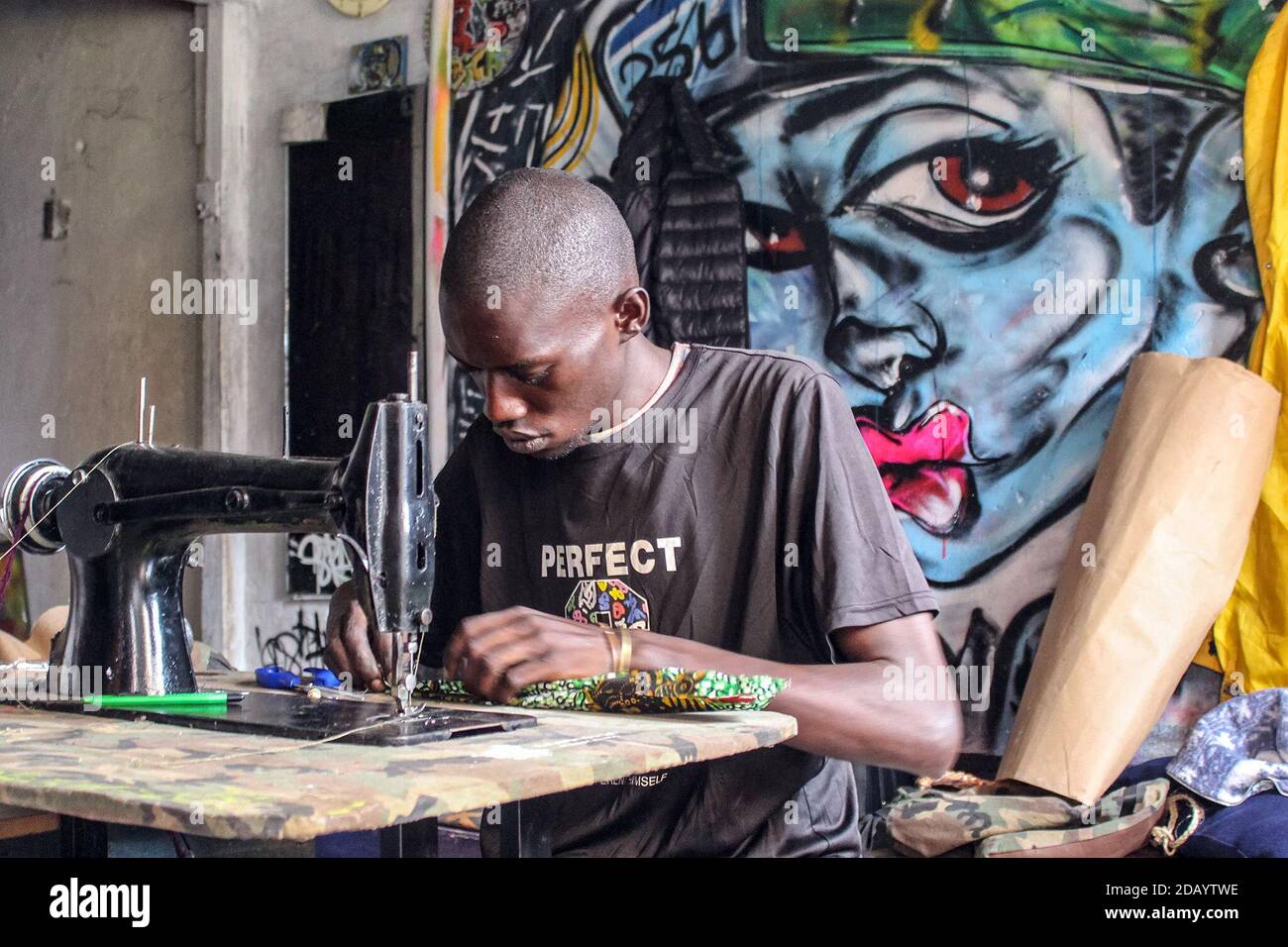 Obbo Lawrence cita materiali per fare uno zaino in uno studio chiamato  Banakibuga Street Minds, che condivide con altri 7 artisti a Kampala,  Uganda. Lawrence mescola tessuti converse e africani per realizzare