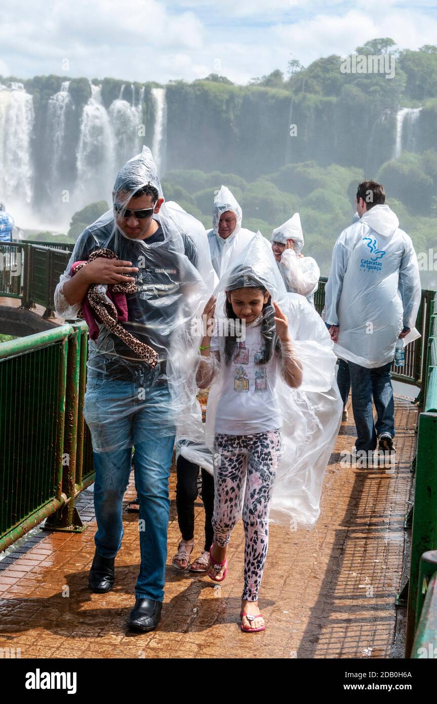 I visitatori che indossano i mac in plastica acquistati dallo spray causato da Le cascate vicine sul passaggio pedonale sul lato brasiliano Delle cascate di Iguazu i Foto Stock