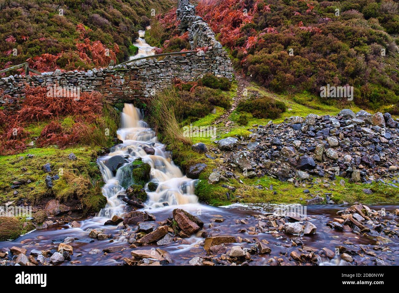 Un piccolo fiume che scorre attraverso un muro di pietra a secco in discesa Foto Stock