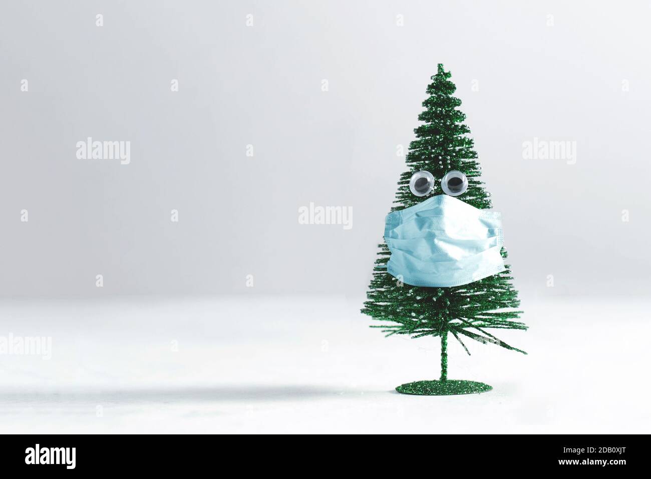 Piccolo pinetree dell'albero di Natale con gli occhi che indossano un protettivo blu maschera chirurgica Foto Stock