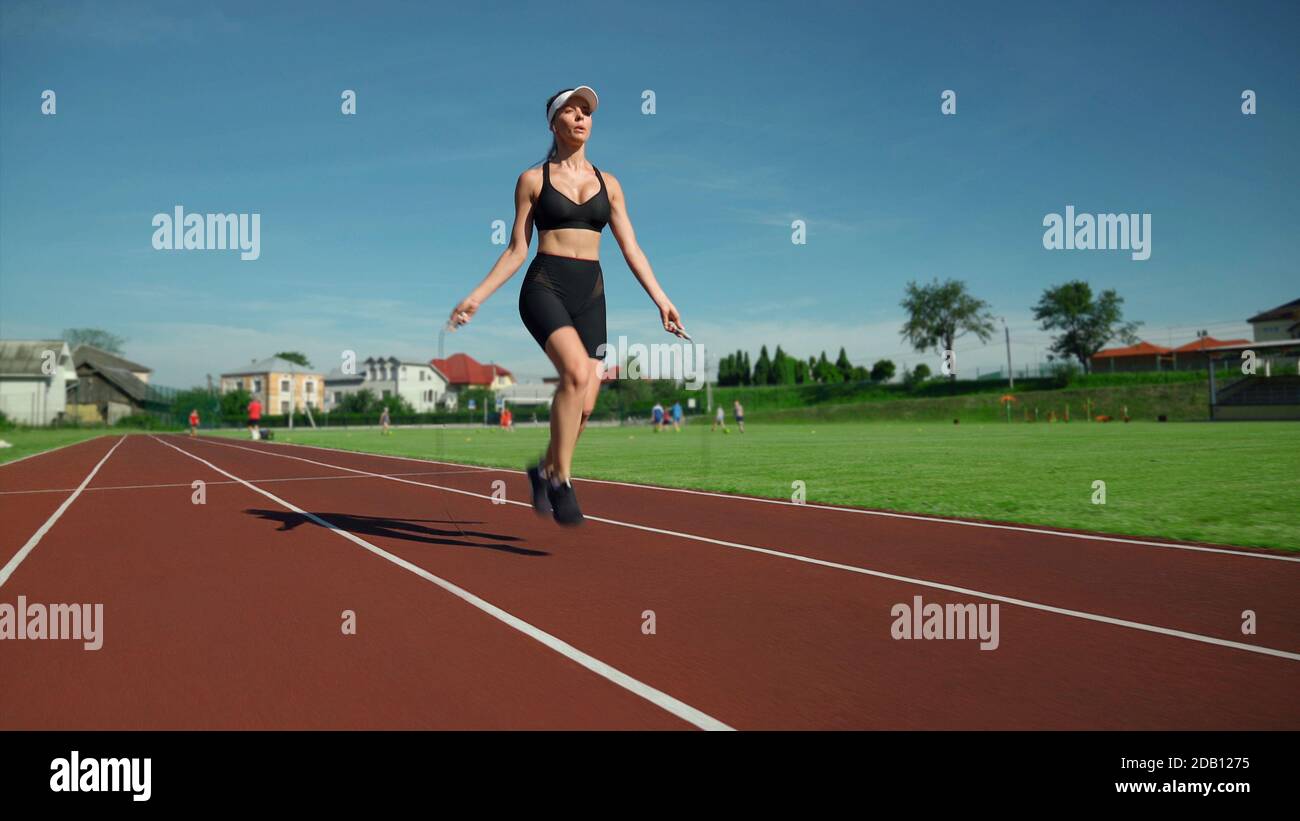 Vista laterale di una splendida giovane donna muscolare con cappuccio bianco e sportswear nero che pratica esercizi di riscaldamento allo stadio. Movimento di ragazza di misura che salta usando la corda saltante all'aperto. Foto Stock