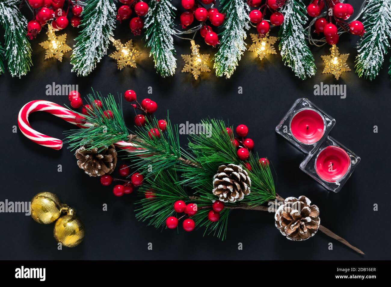 Decorazioni dell'albero di Natale su uno sfondo scuro. Umore invernale, bacche agile, cono di pino, ramo di abete rosso con neve su lavagna. Cartolina festiva con lucido Foto Stock