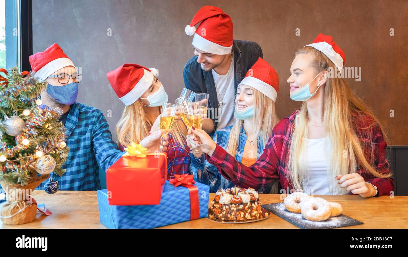 Gruppo di felici giovani amici con maschere facciali festeggiano il Natale insieme bere champagne in casa isolamento Foto Stock