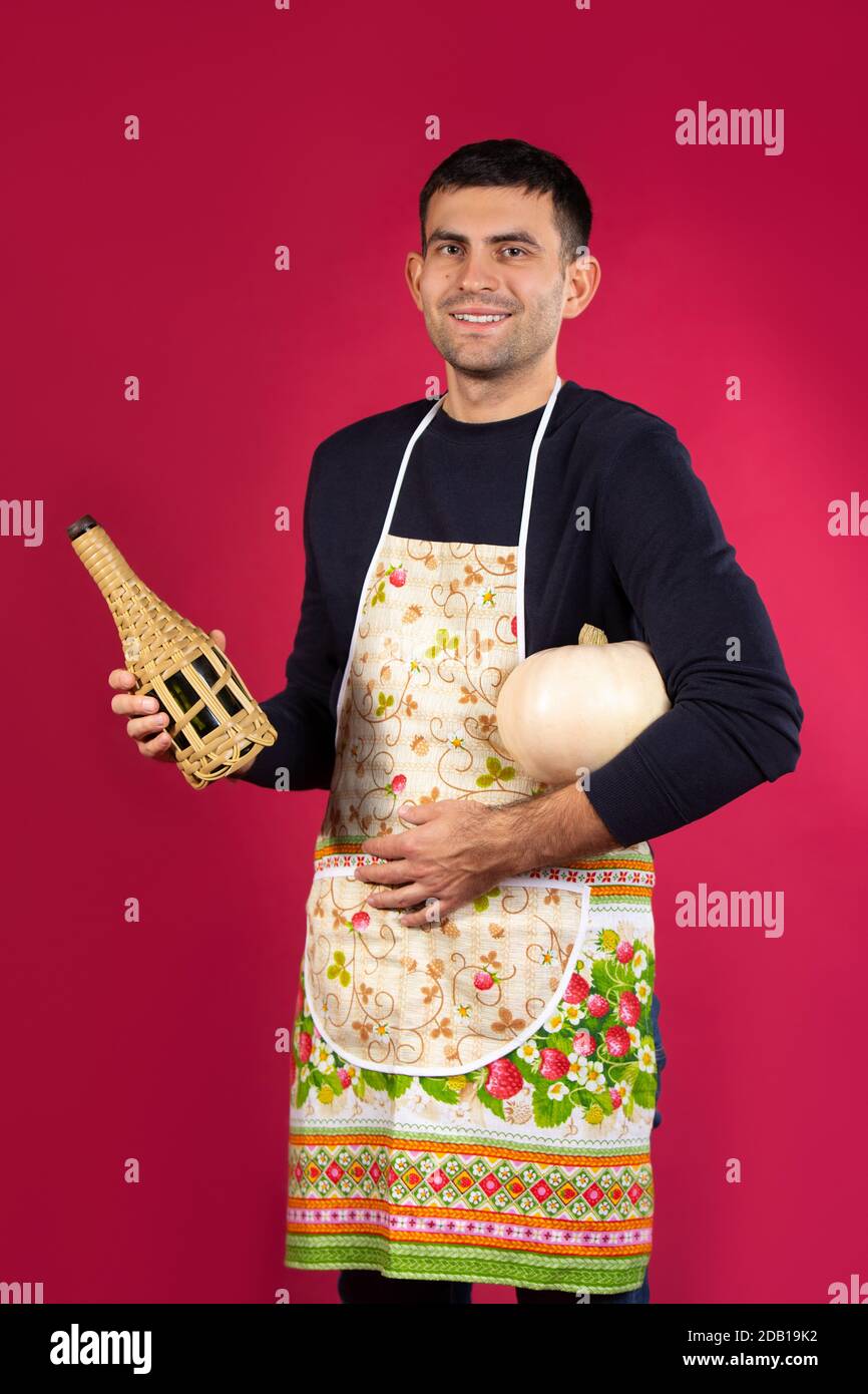 Un uomo sorride dopo aver cucinato la cena e si posa con la sua bevanda scelta. Il concetto di stereotipi di genere. Foto su sfondo rosa. Foto Stock