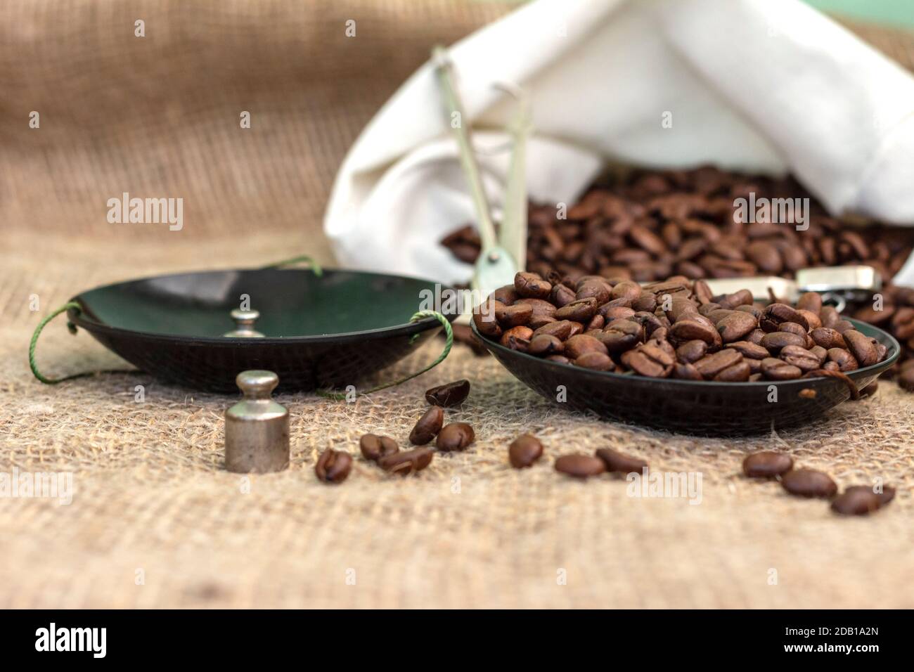 Chicchi di caffè arrosto, pesati su un'antica bilancia a mano con pesi, adagiati su un tavolo coperto di burlap. Foto Stock