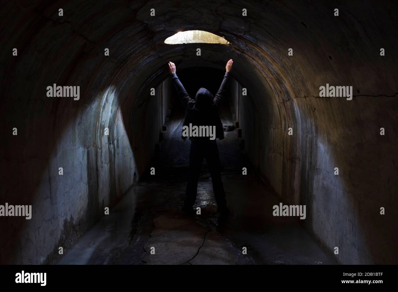 Un uomo in un tunnel sotterraneo scuro sta cercando una via d'uscita e solleva le mani al cielo chiedendo aiuto. Foto Stock