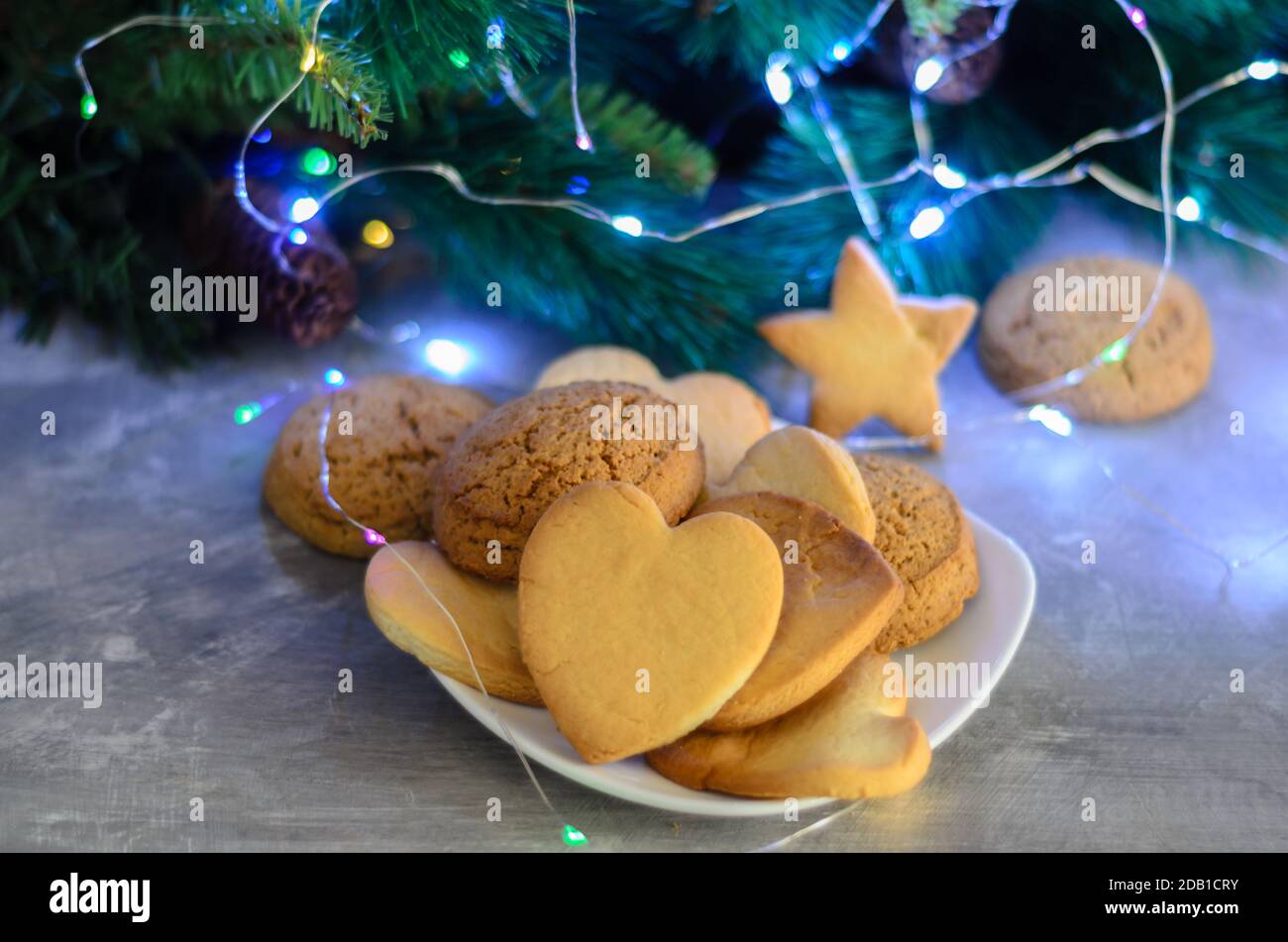 Biscotti fatti in casa a forma di cuore in un piatto bianco sullo sfondo delle decorazioni natalizie. Messa a fuoco selettiva. Foto Stock