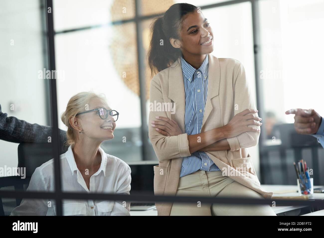 Due diverse colleghe sorridenti che guardano da parte mentre hanno un incontro con i colleghi nell'ufficio moderno Foto Stock
