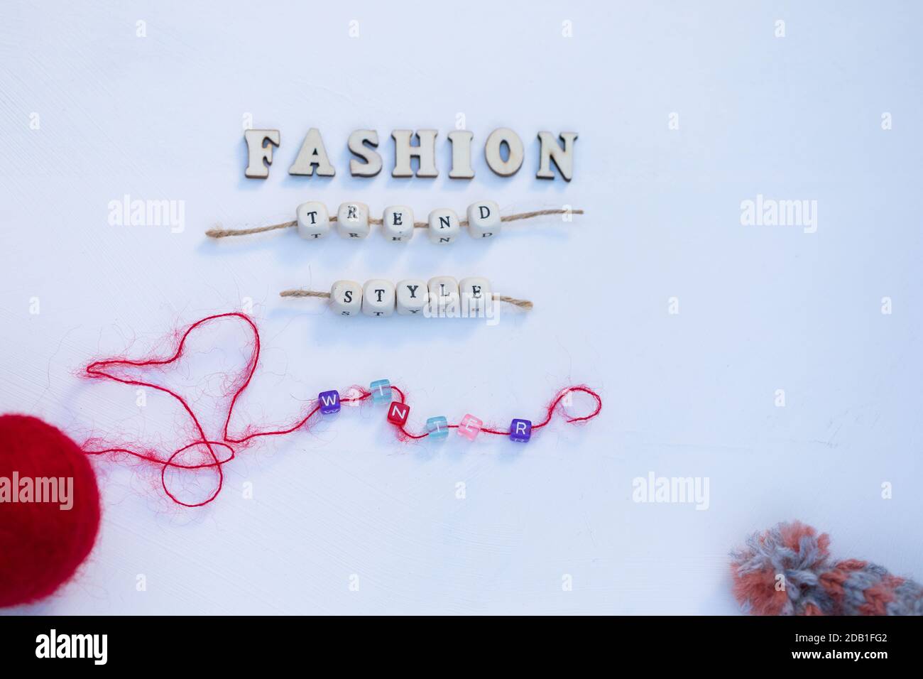 Red Ball of Wool, Warm Hat with Pompom e Words Fashion Trend Style Winter sono su legno bianco sfondo. Vista dall'alto. Foto Stock