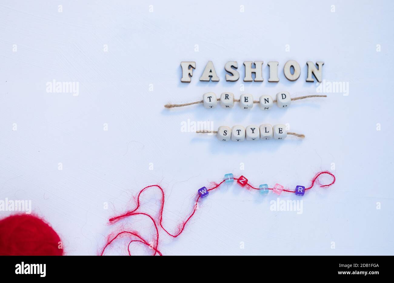 Parole stile tendenza moda Inverno e rosso ornamenti con palla di lana sono su legno bianco sfondo, Copy Space. Vista dall'alto composizione minima. Foto Stock