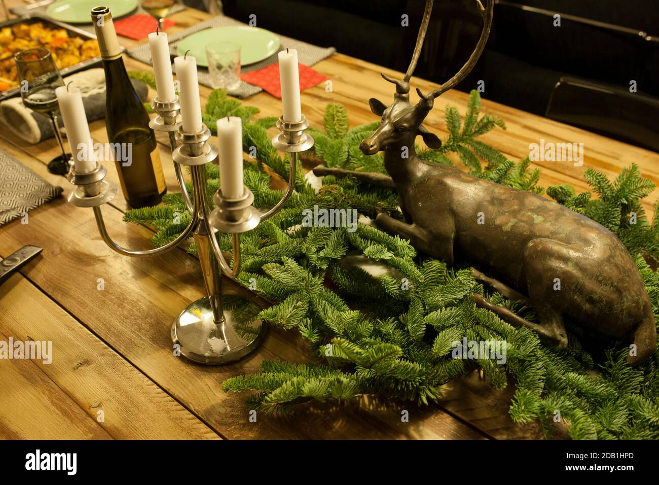 Cena di Natale su un tavolo di legno con rami di pino, un lampadario e una bottiglia di vino rosso Foto Stock