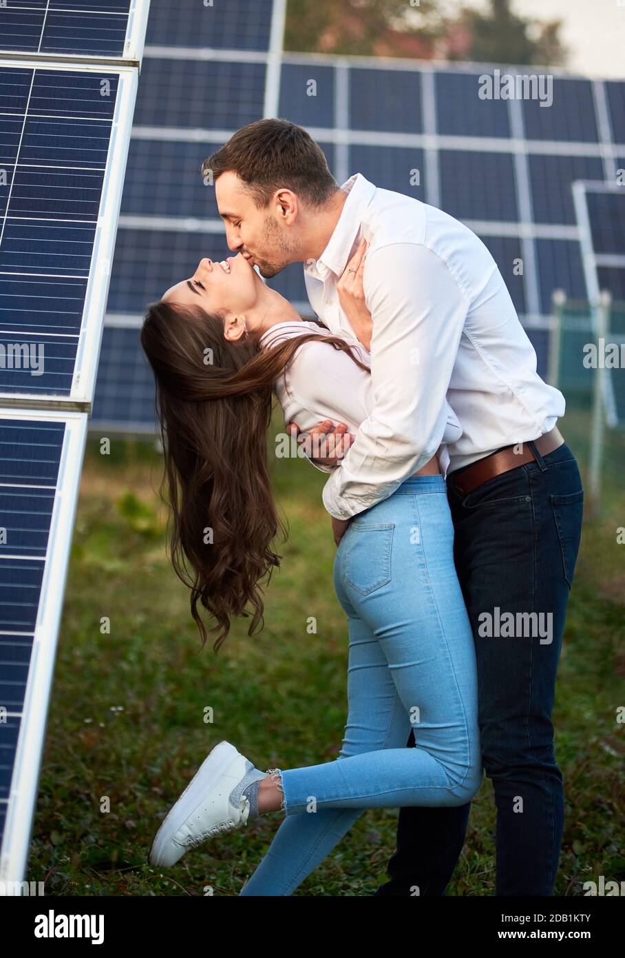 Un uomo bacia il suo amante sullo sfondo di una serie di pannelli solari. Una donna dai capelli lunghi sta godendo le braccia di una persona amata. Un mondo moderno con tecnologia in continua evoluzione Foto Stock