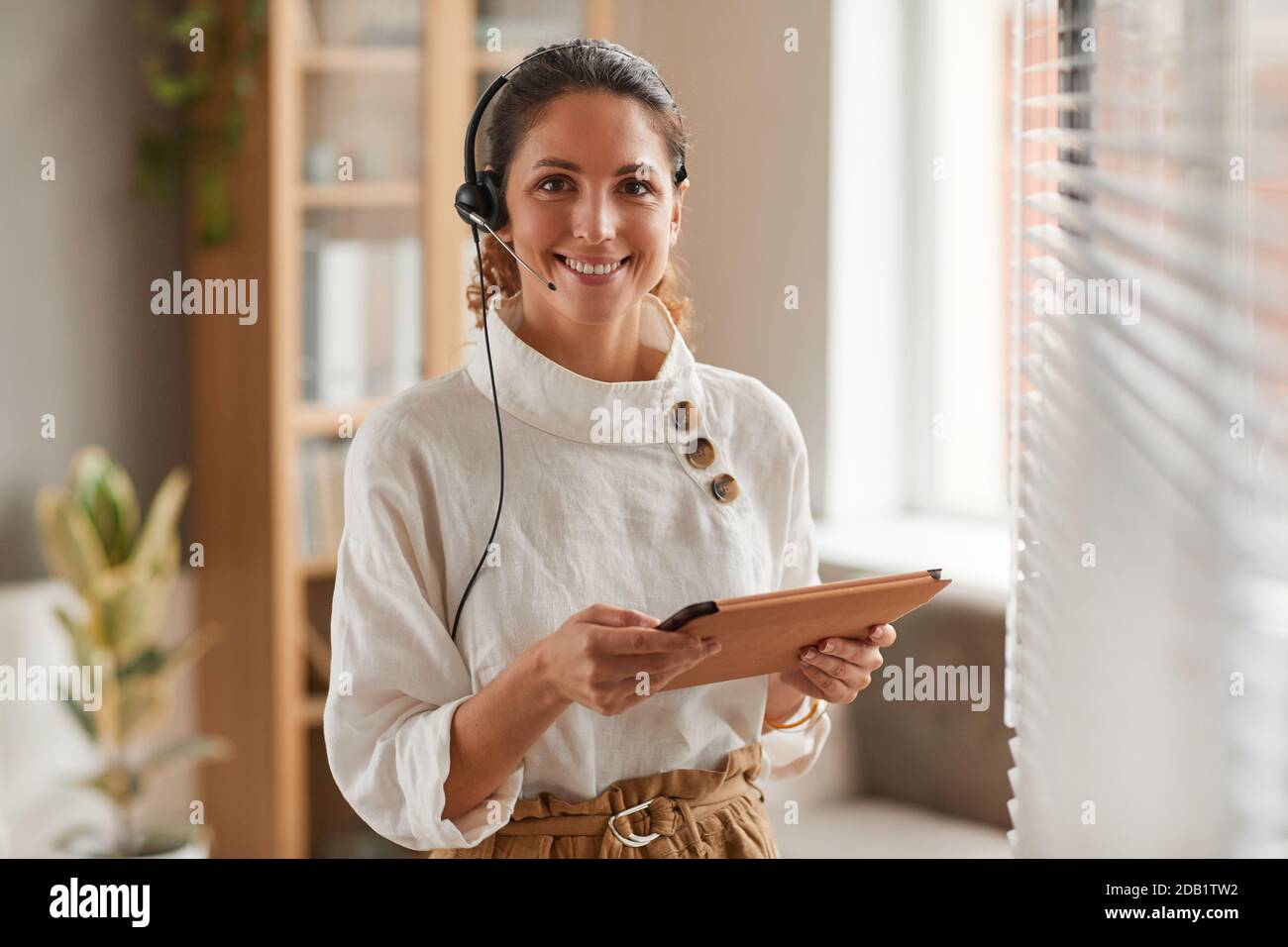Ritratto in vita di una donna d'affari sorridente che indossa le cuffie e guarda la fotocamera durante la riunione online in ufficio, spazio per la copia Foto Stock