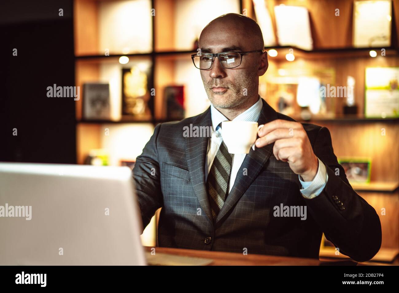 Uomo d'affari di successo legge le notizie del mondo. Il maschio di media età guarda sullo schermo del computer portatile bevendo caffè mentre lavora in un business center o in un hotel Foto Stock