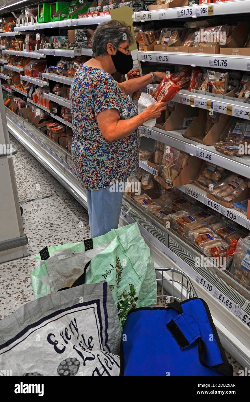 Tesco store senior maturo cliente di acquisto donna indossando Covid 19 coronavirus maschera di acquisto per cibo tenendo lista nel supermercato Aisle England UK Foto Stock