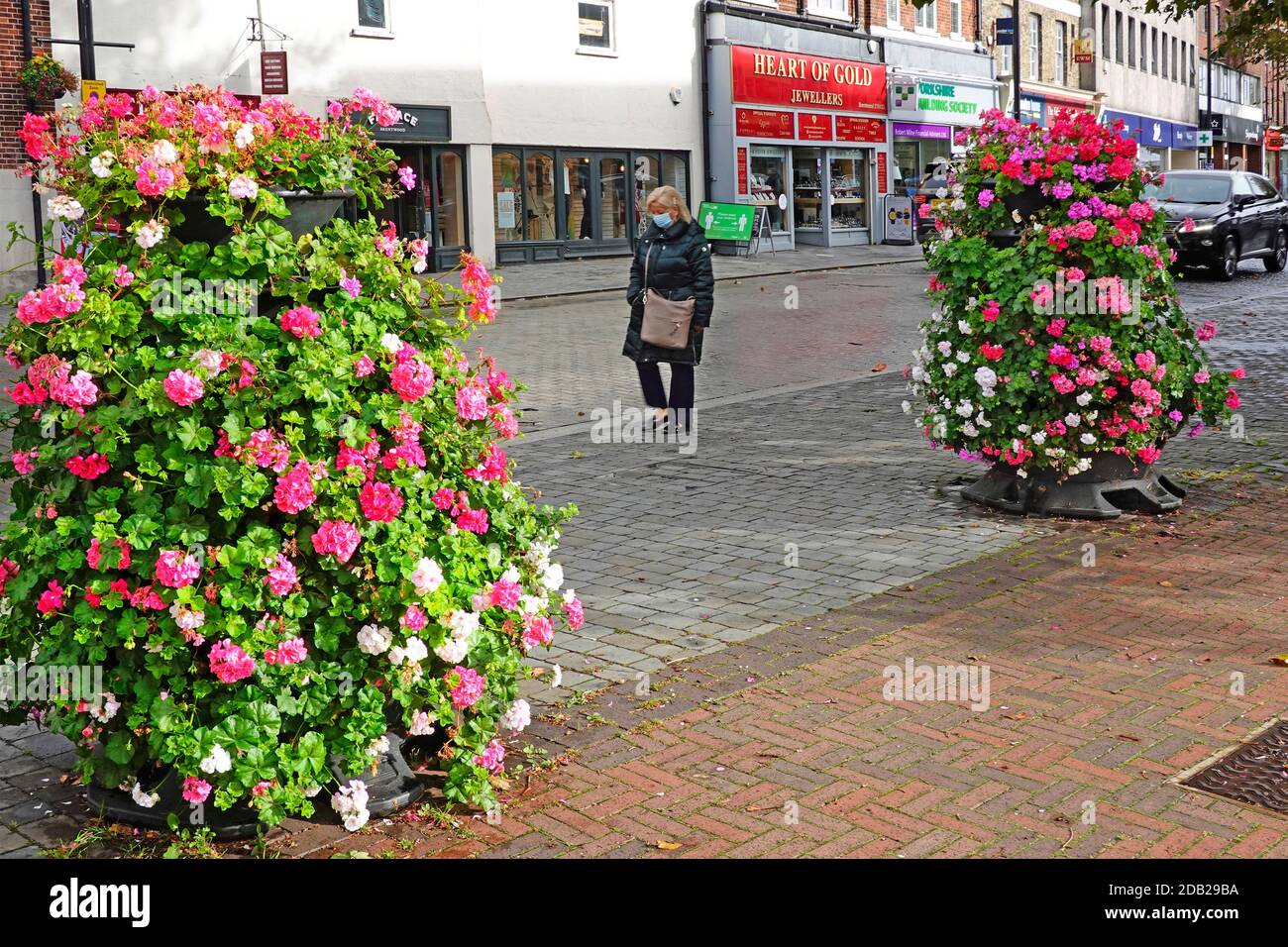 Donna che indossa la maschera di Coronavirus Covid 19 che cammina da sola lungo Vicino deserta Brentwood shopping alta strada tra Essex mostra fiori Inghilterra Regno Unito Foto Stock