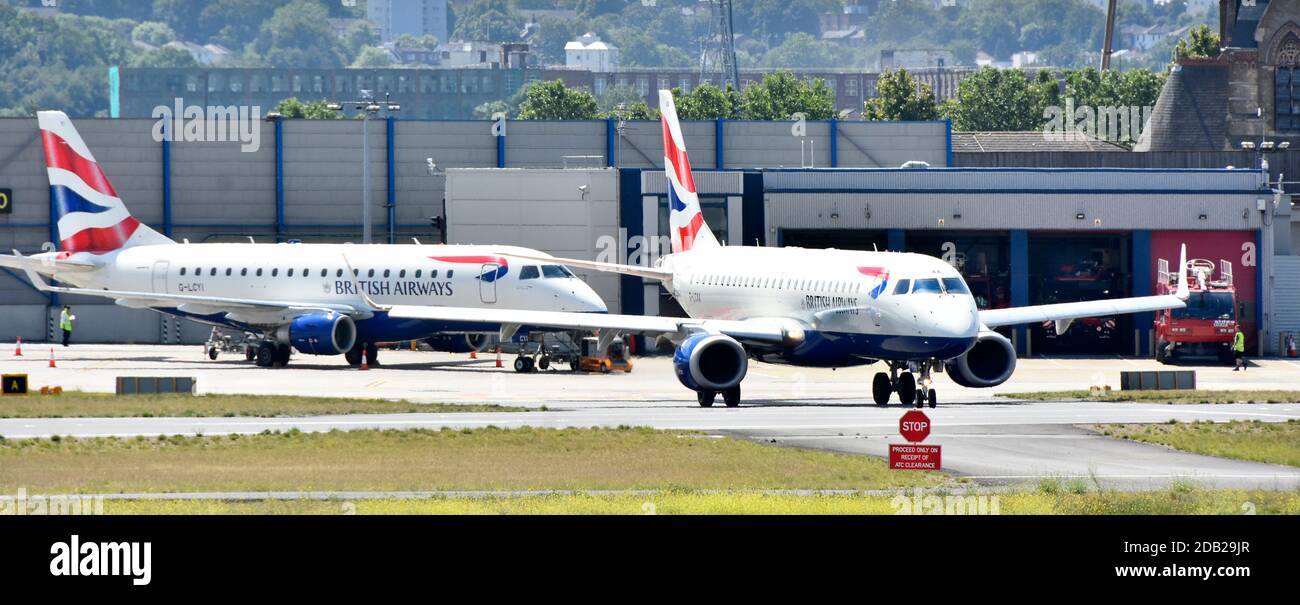 British Airways Jet Planes 1 che tassano all'aeroporto di London City Di fronte all'edificio della stazione dei vigili del fuoco e alle apparecchiature di emergenza Newham East London Inghilterra Regno Unito Foto Stock
