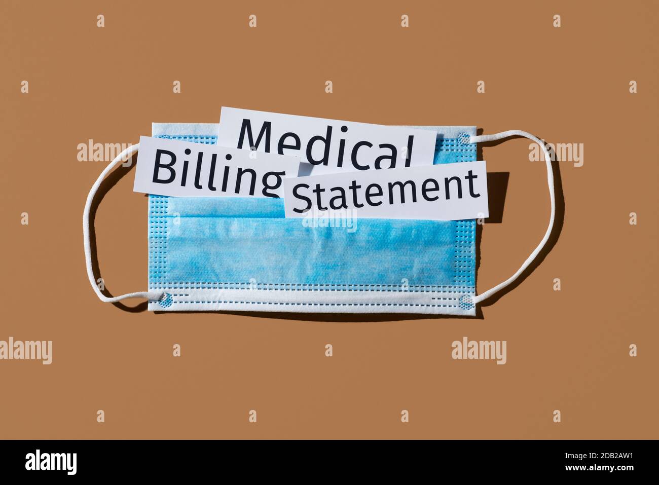 una maschera chirurgica blu e la dichiarazione di fatturazione medica di testo su sfondo marrone Foto Stock