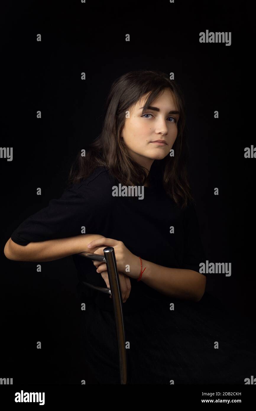 Ritratto di una ragazza di quindici anni su sfondo nero, una ragazza annebbiata sul retro di una sedia Foto Stock