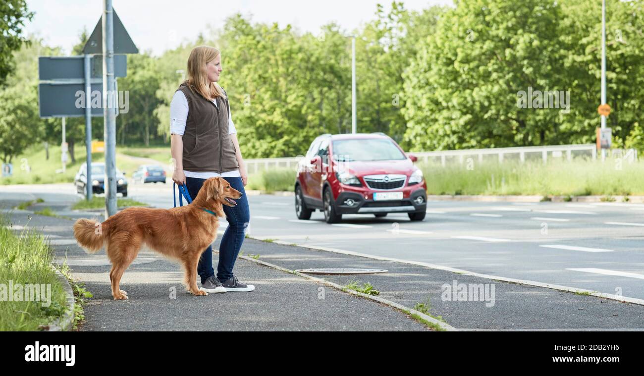 Donna e cane di razza mista in piedi su un marciapiede vicino a una strada. Non per guide animali fino al 9/2022 Foto Stock