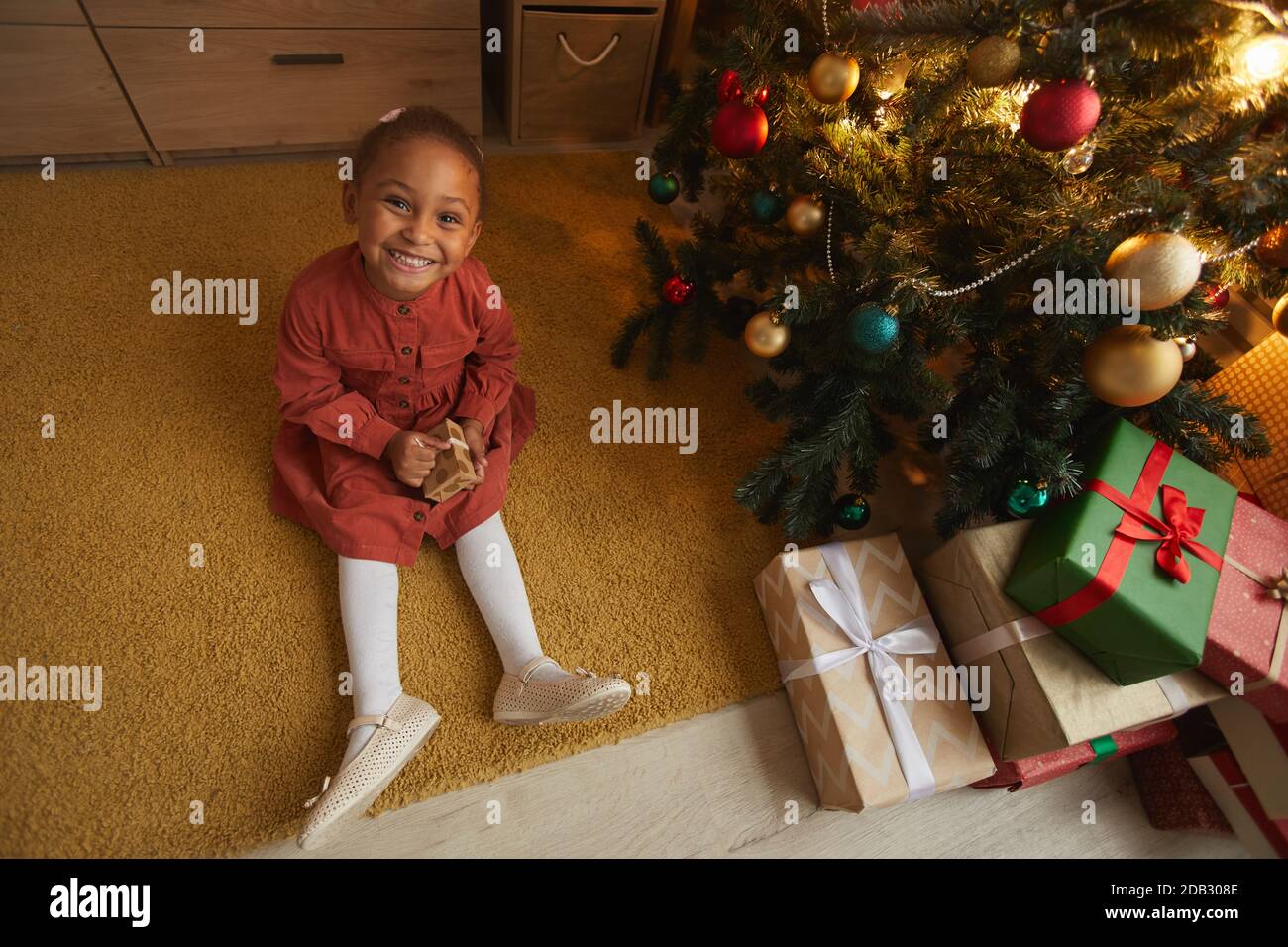 Sopra la vista ritratto di eccitato afroamericana ragazza apertura regali di Natale mentre si siede da albero a casa e sorridendo a macchina fotografica, copia spazio Foto Stock
