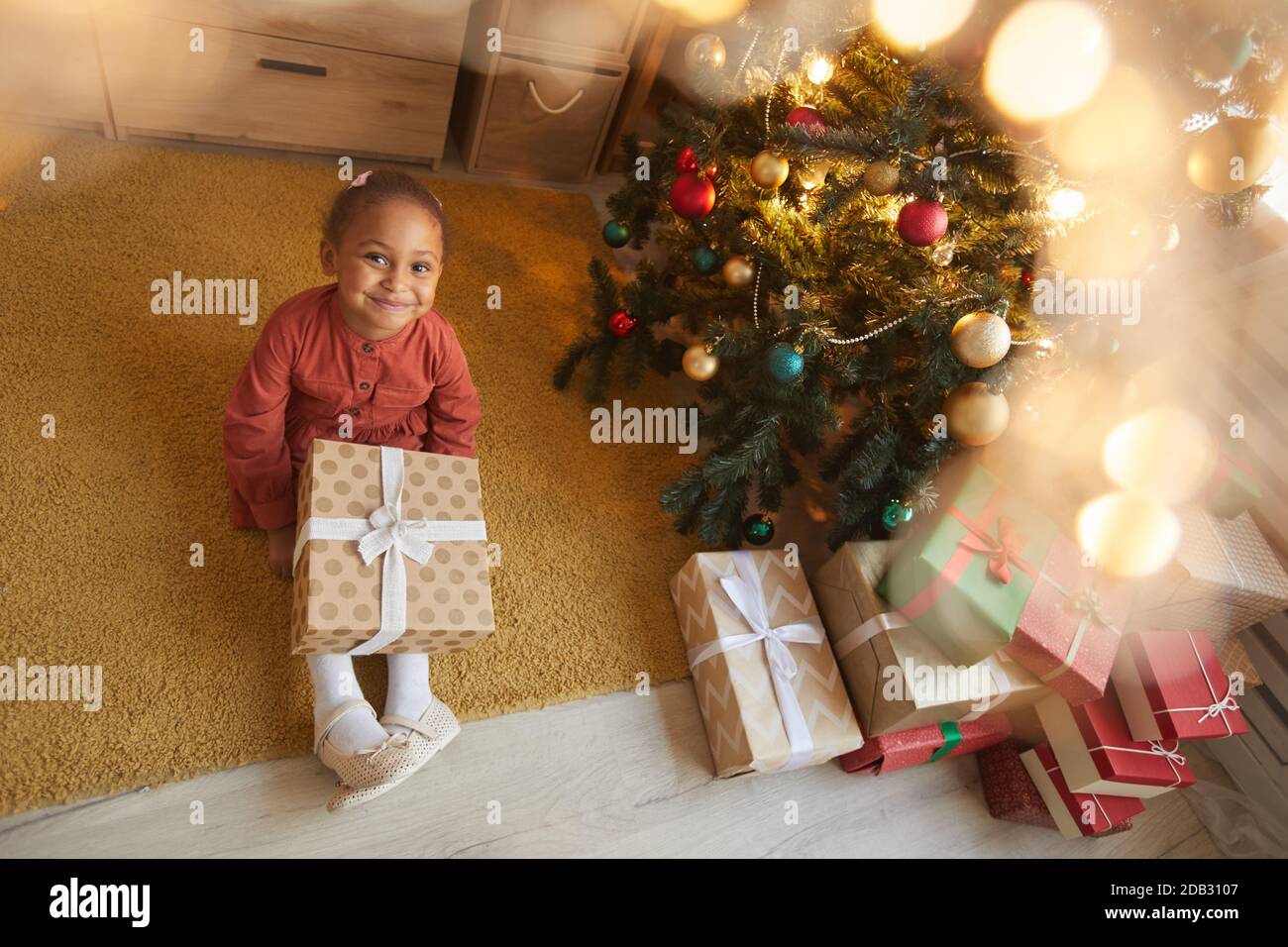 Sopra la vista ritratto di felice afroamericana ragazza apertura regali di Natale mentre si siede da albero a casa e sorridendo a macchina fotografica, copia spazio Foto Stock