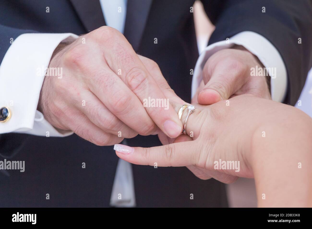 Marito con abito scuro e moglie con abito luminoso scambiano anelli di lusso dorati. Tenere le mani e mettere un anello su un dito l'altro. Foto Stock