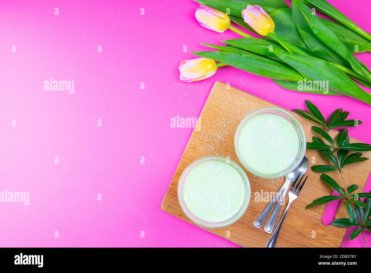 Yogurt al limone alla menta con kiwi in ciotole per insalata su tavola di legno insieme a tulipani su sfondo rosa. Foto Stock