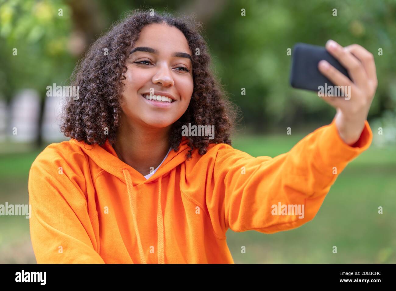 Bella felice mista razza Africana americana giovane donna adolescente femmina bambino sorridente con denti perfetti scattando foto selfie all'aperto con c Foto Stock