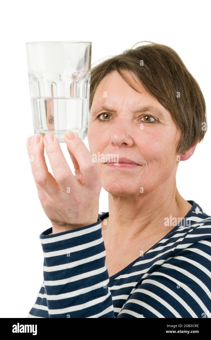 Vista testa e spalle di una donna matura che guarda scetticamente a un bicchiere pieno d'acqua, su sfondo bianco. Foto Stock