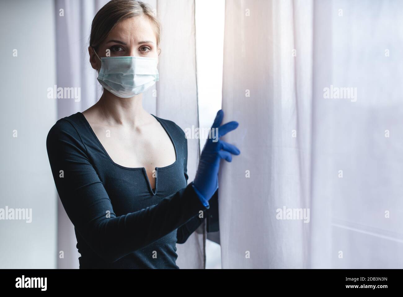 Annoiata donna in quarantena corona o sotto coprifuoco che guarda fuori dalla finestra per la strada Foto Stock